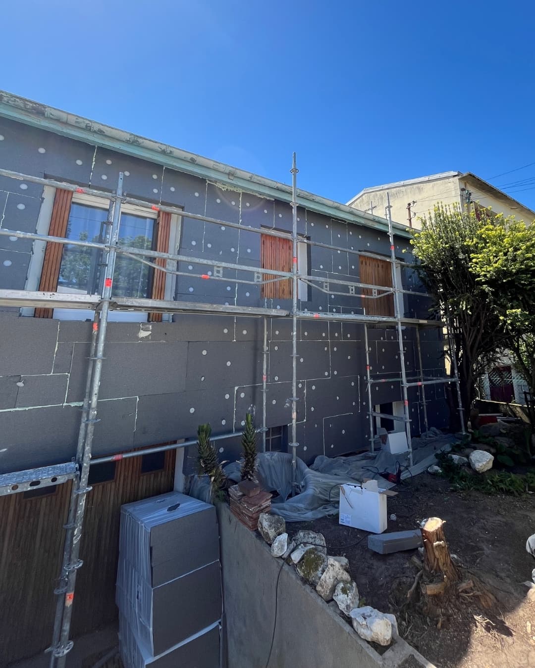 Chantier d'isolation thermique par l'extérieur à Taverny : vue de face avec échafaudage en place. Les ouvriers fixent les panneaux isolants en polystyrène gris sur la façade.