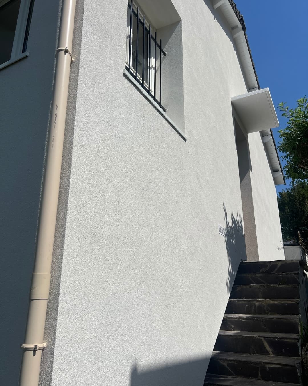 Vue détaillée de l'angle d'une maison après ITE, montrant la qualité de finition de l'enduit blanc sec sur le mur et l'escalier extérieur rénové à Taverny.