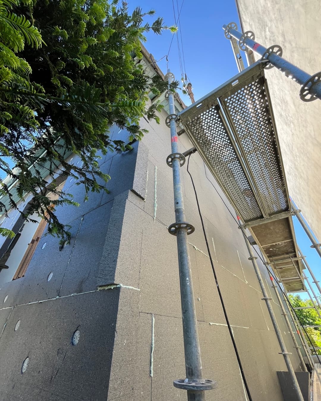 Vue technique d'un chantier ITE par KS Rénov : pose en cours des panneaux isolants gris, fixés par calage et chevillage. Échafaudage visible à droite.