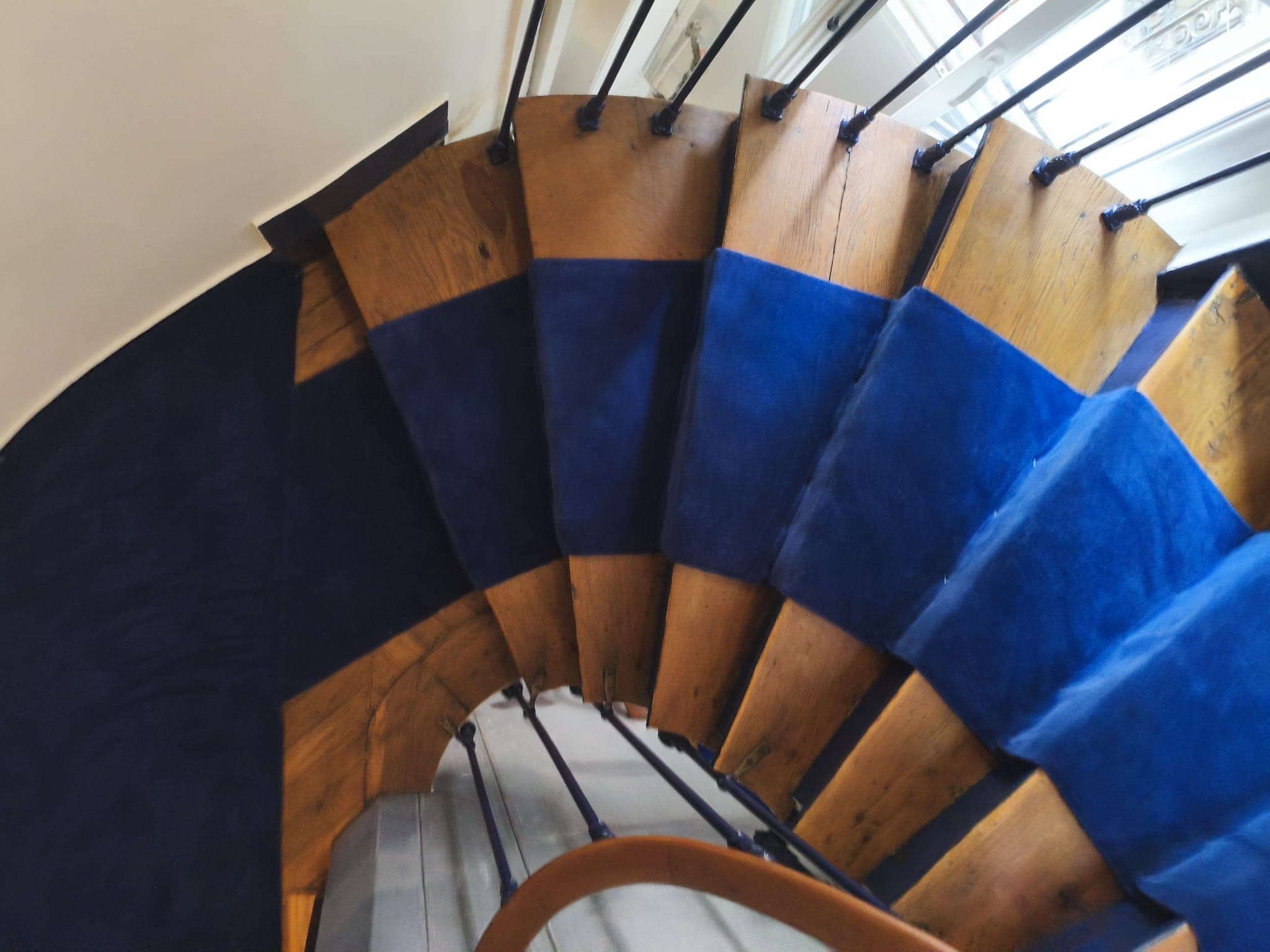 Vue en plongée d'un escalier tournant à Paris 18e, illustrant la découpe sur mesure du tapis de passage bleu sur le bois vitrifié.