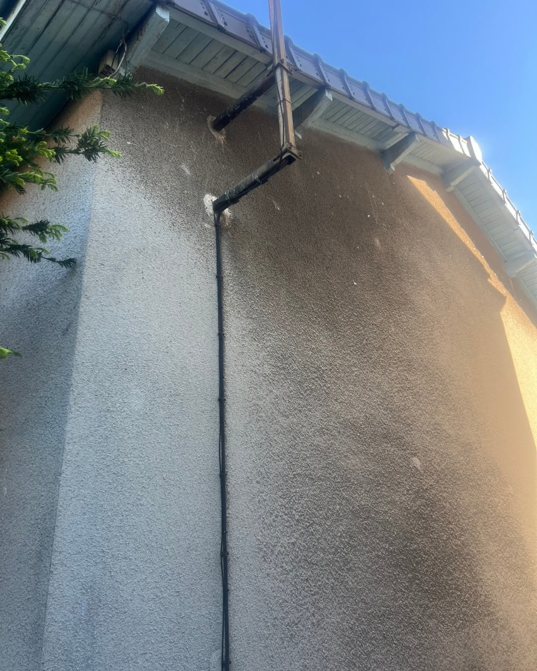 Vue rapprochée du pignon d'une maison à Taverny avant travaux d'isolation, montrant un enduit ancien et des conduits extérieurs. Phase de préparation du support.