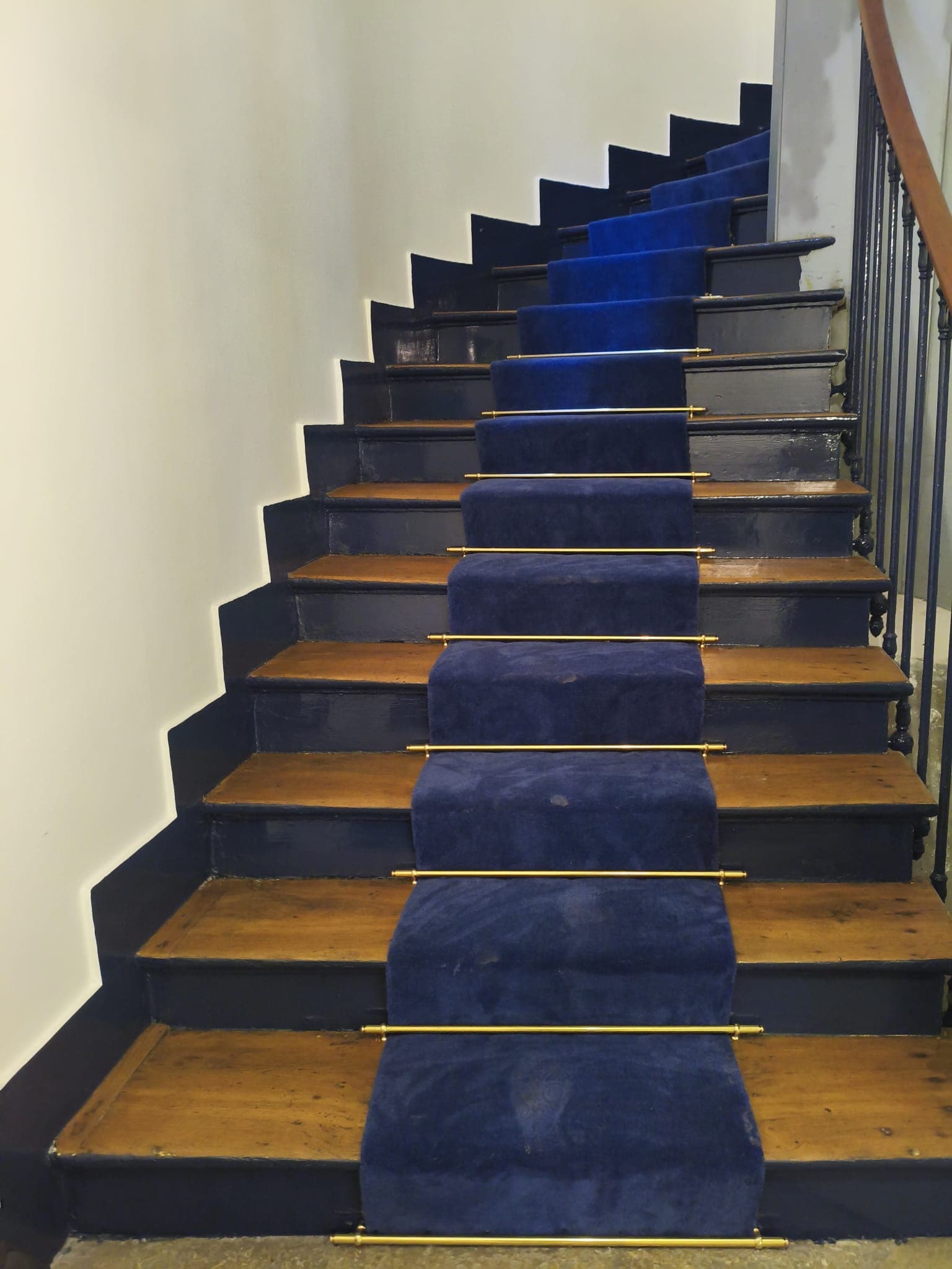 Escalier en bois massif rénové par KS RENOV avec peinture bleu nuit sur les côtés et pose d'un chemin d'escalier fixé par des barres en laiton.